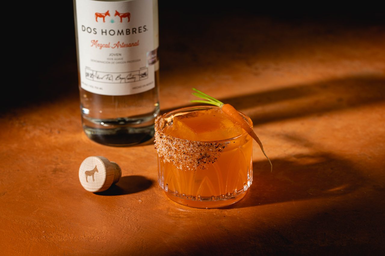 Dos Hombres Mezcal bottle with Sweet Lips cocktail featuring chili salt rim and carrot garnish